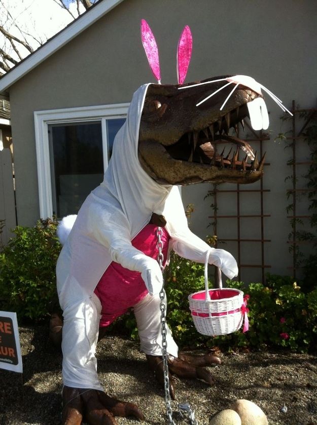 a man dressed as a t - rex holding a basket with easter eggs in front of a house