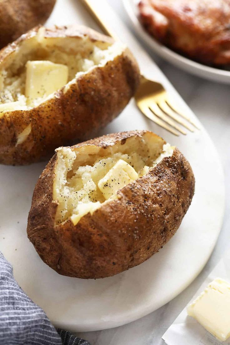 two baked potatoes with cheese and butter on a plate