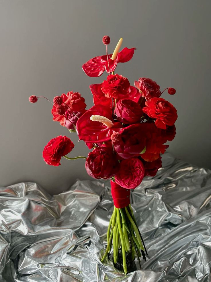 a bouquet of red flowers sitting on top of tinfoil covered table cloth, next to a gray wall