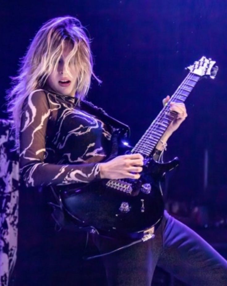 a woman holding a guitar while standing on stage