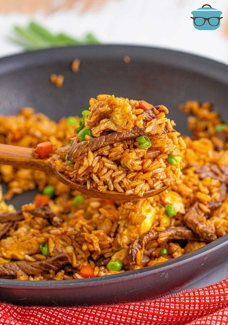 a spoon full of rice with meat and peas in it on a plate next to a red napkin