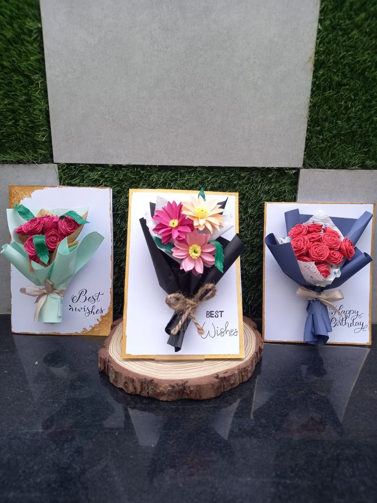 three greeting cards with flowers on them sitting on top of a black table next to a tree stump