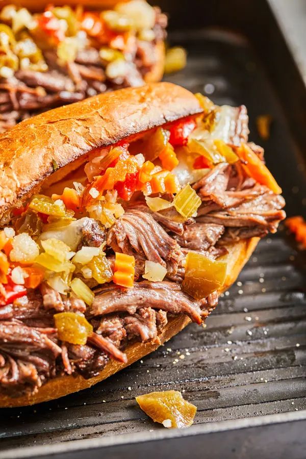 two sandwiches with meat, peppers and onions on top of a baking sheet in an oven