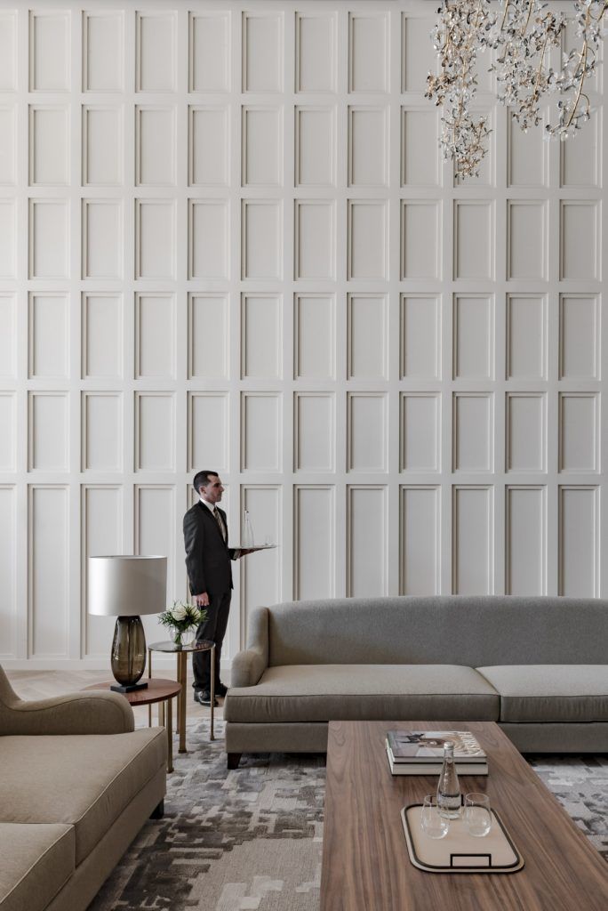 a man in a suit standing next to a couch and coffee table with a lamp on it