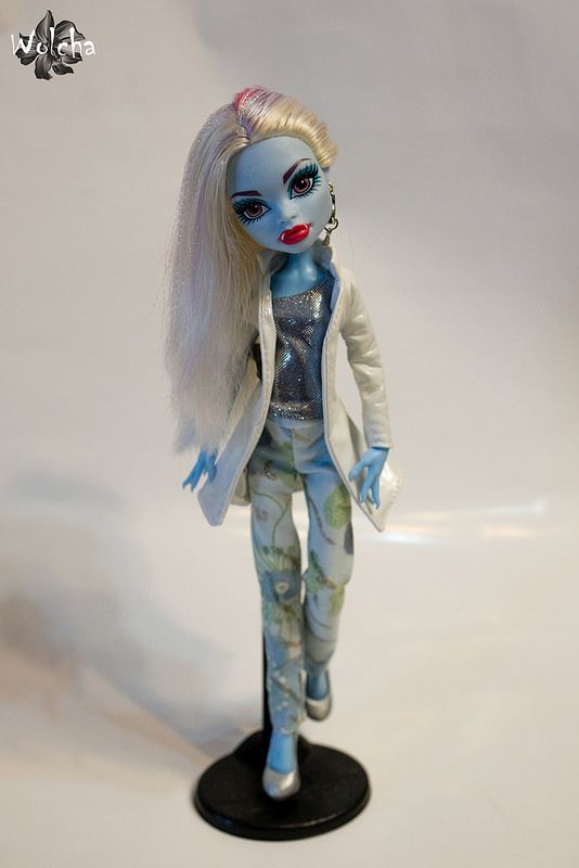 a doll with white hair and blue skin is standing on a black base, wearing a white blazer