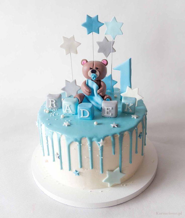 a blue and white birthday cake with a teddy bear on it's top is decorated with stars