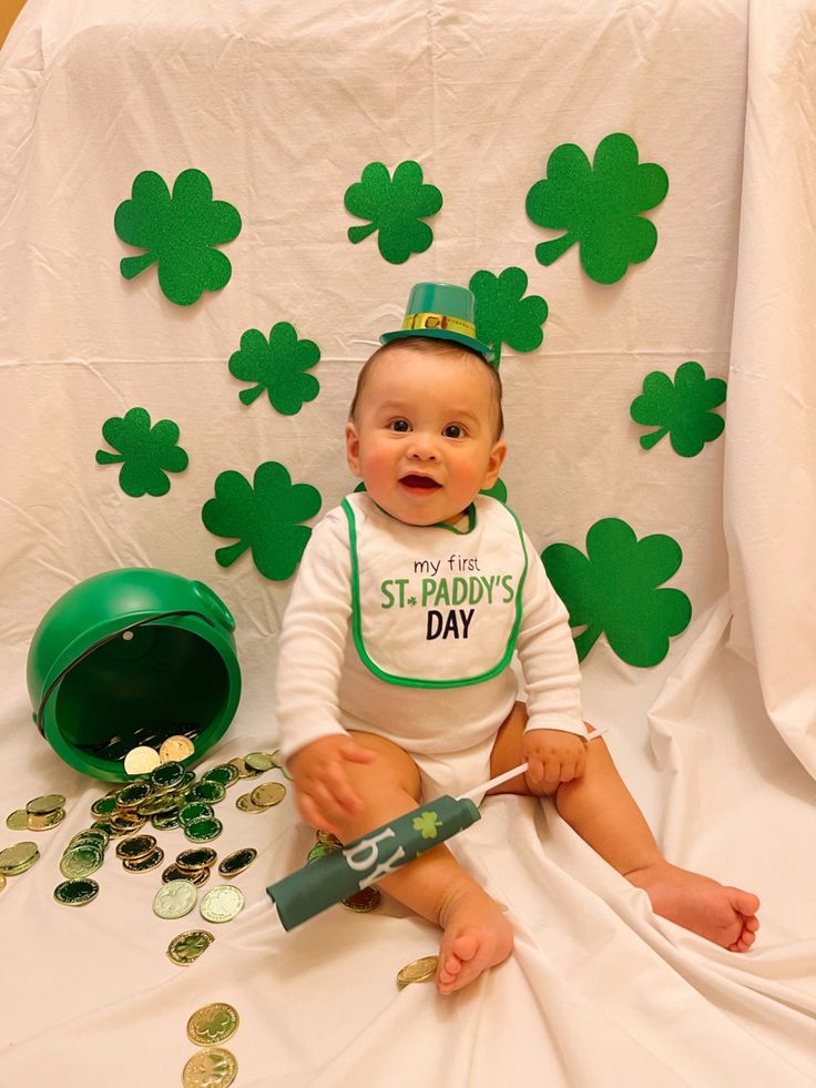 a baby sitting on the floor with green shamrocks around him and his st patrick's day hat