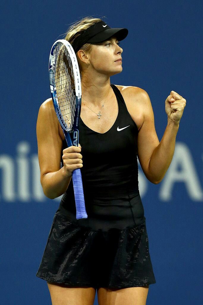 a woman holding a tennis racquet on top of a tennis court in front of a blue wall