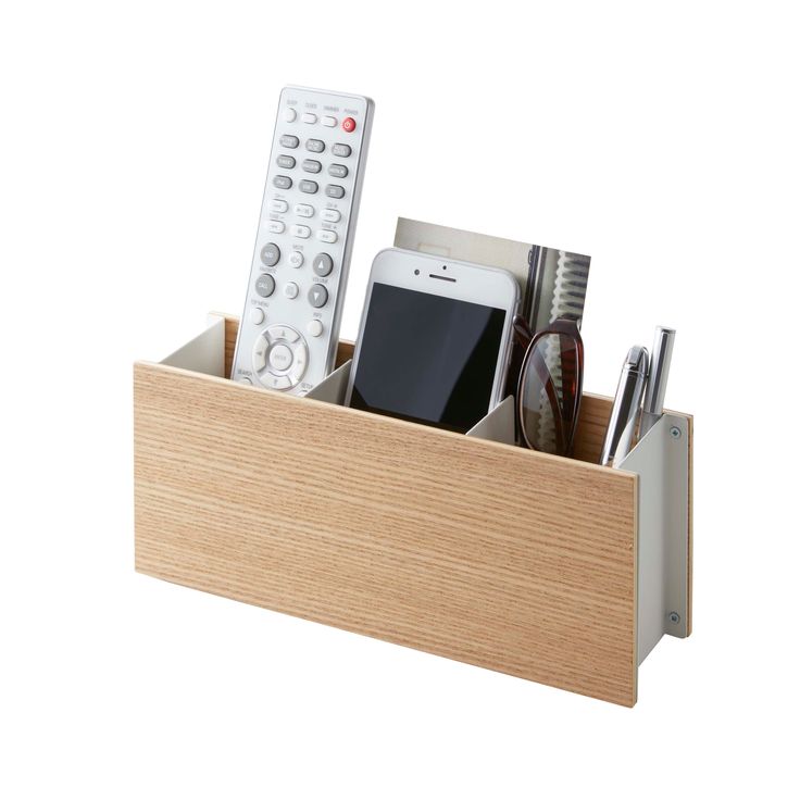 a cell phone, remote control and pens in a wooden holder on a white surface