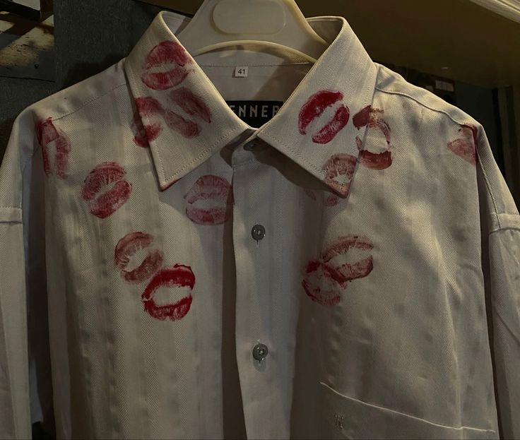 a white shirt with red lipstick prints on the collar and chest, hanging from a hanger