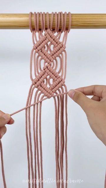 two hands are working on a piece of pink yarn