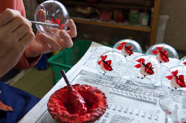 a person holding a glass ball with red flowers on it and some wine glasses in front of them