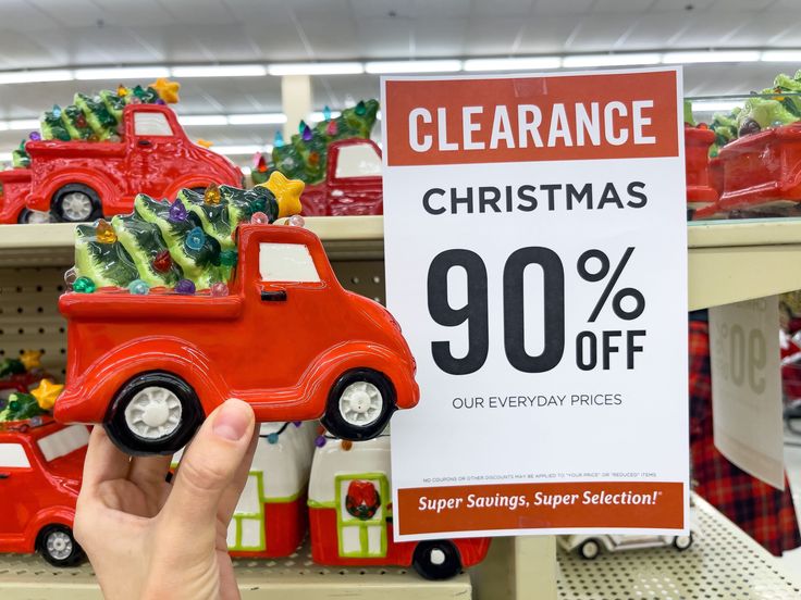 a hand is holding up a christmas sale sign in front of some toy cars and trees