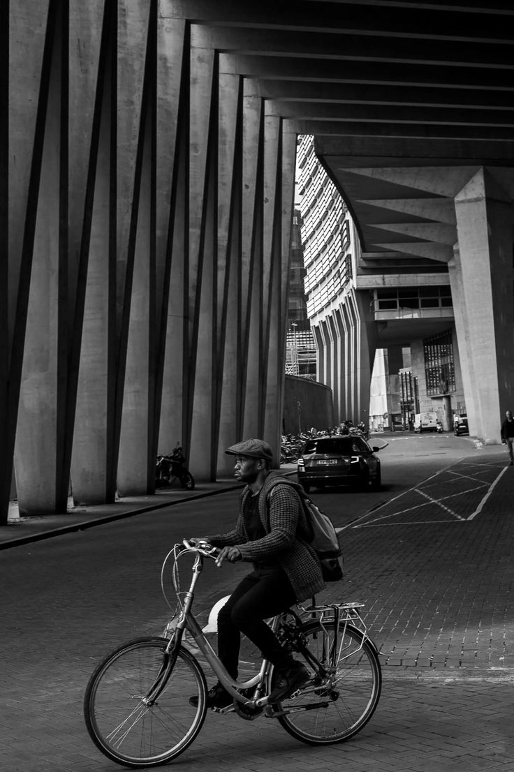 a man riding a bike down a street under an overpass in black and white