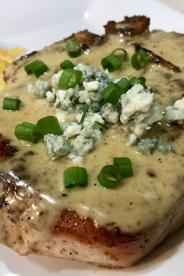 a white plate topped with meat covered in gravy and green onion garnish