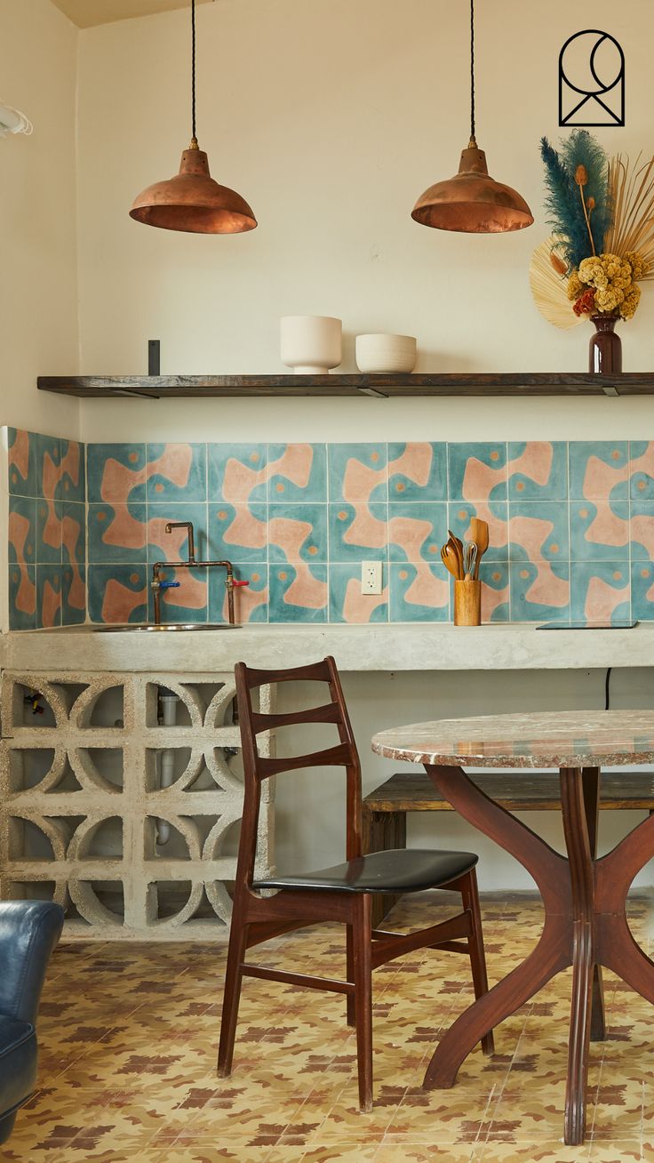 a table and chairs in a room with blue tiles on the wall behind them, along with two hanging lights