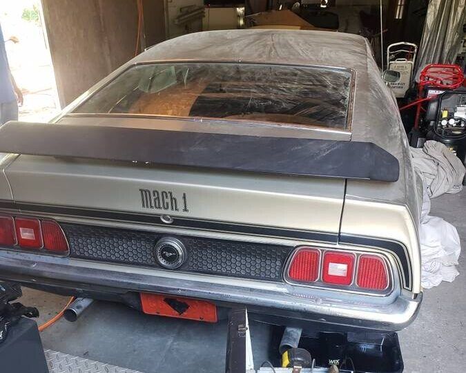 the back end of an old car in a garage with it's hood up