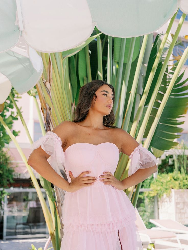 a woman wearing a pink dress standing in front of palm trees