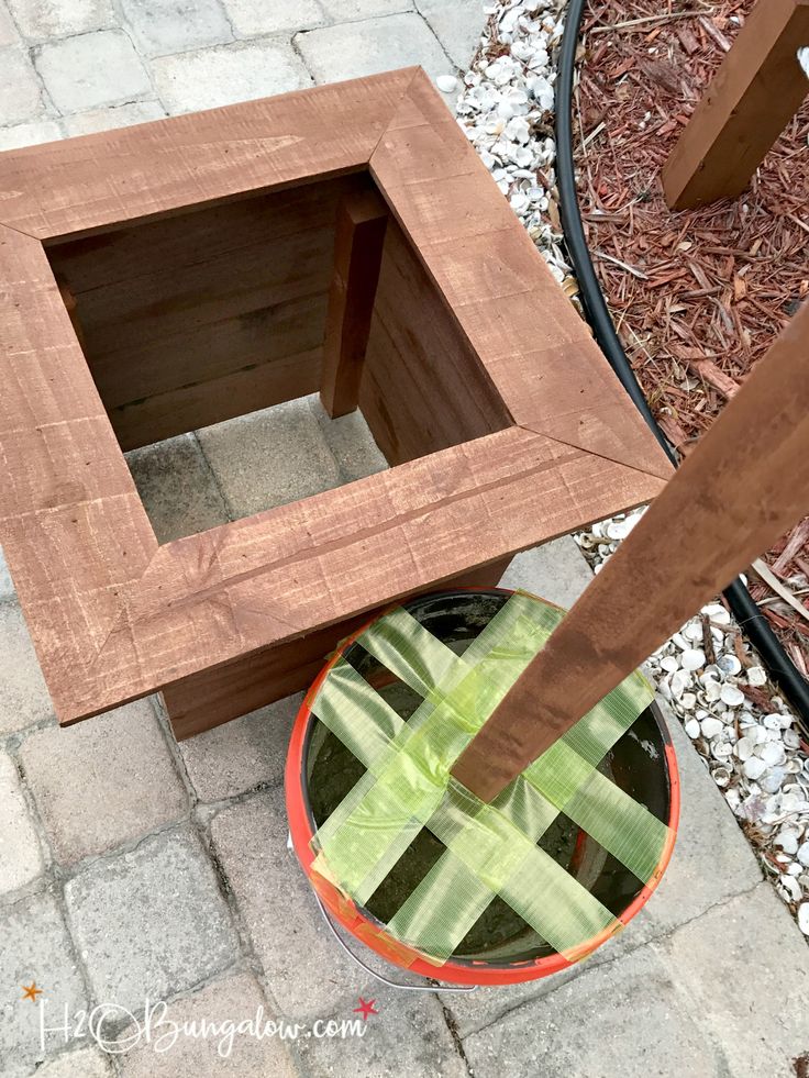 a small wooden box sitting on top of a brick floor next to a planter