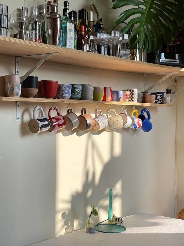 a shelf filled with lots of cups on top of a white counter next to a potted plant