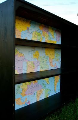 a book shelf with a map on it in the grass next to a street sign