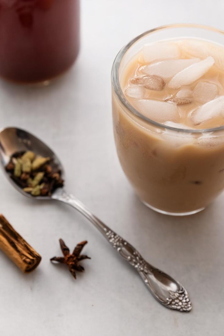 two spoons are sitting next to a cup with ice and cinnamon on it, along with some spices