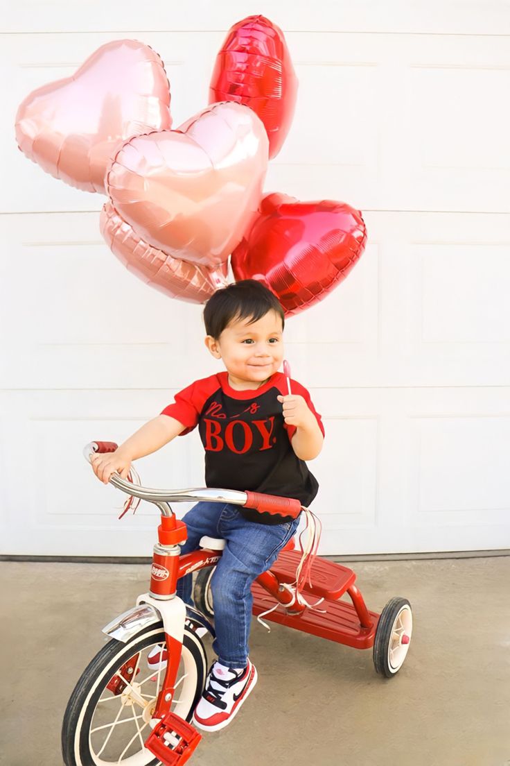 a young boy riding a tricycle with balloons in the shape of hearts