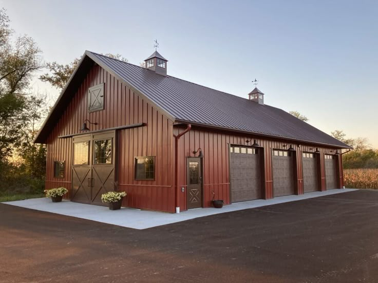 a large red barn with two garages and a clock on the top of it