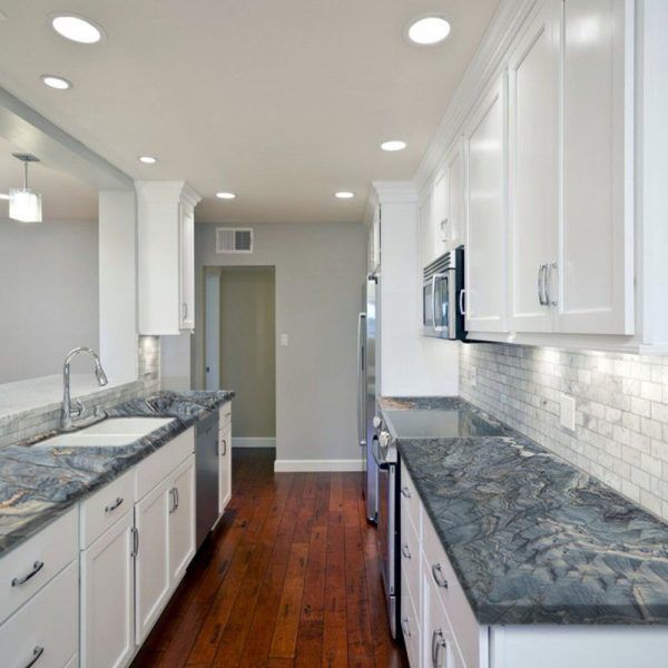 an empty kitchen with white cabinets and marble counter tops, along with hardwood flooring