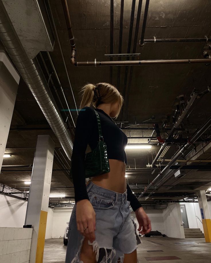 a woman standing in an empty parking garage wearing high waisted shorts and black crop top