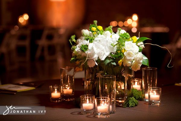 the centerpiece is filled with white flowers and lit candles in glass vases at the head table