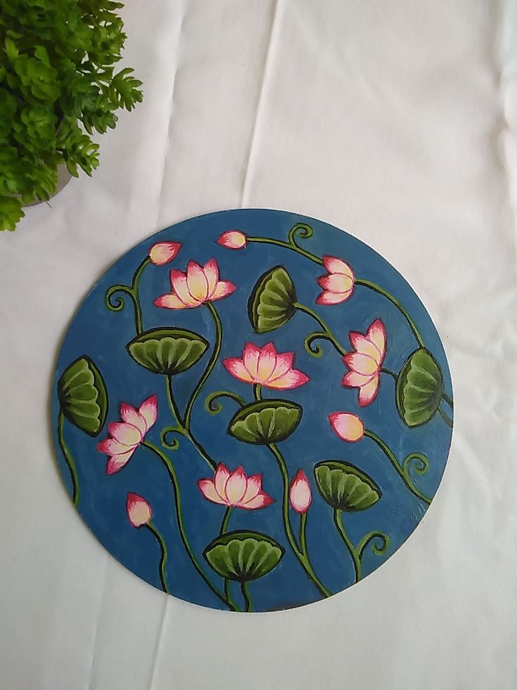 a blue plate with pink flowers and green leaves on it next to a potted plant