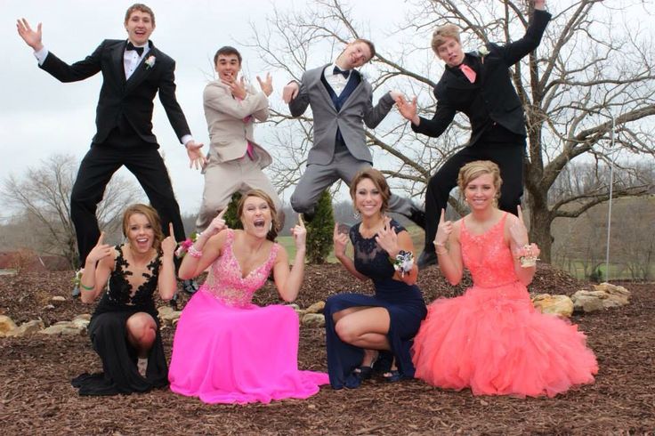 a group of people in formal wear posing for the camera with their hands up and one person wearing a tuxedo