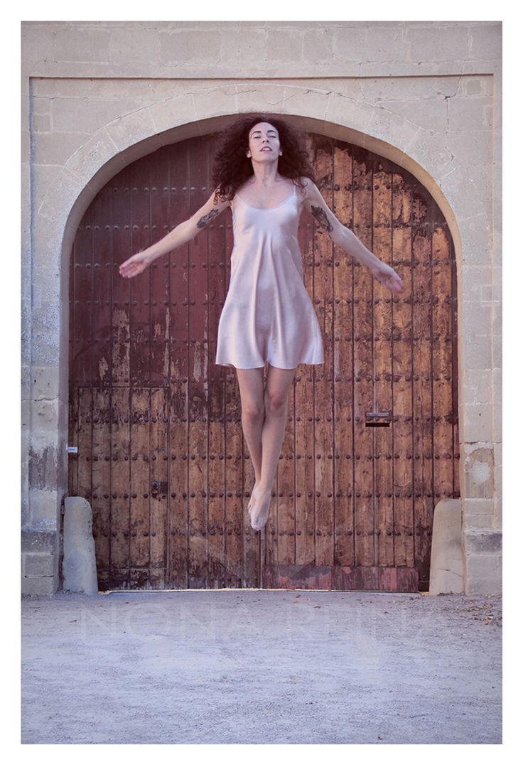 a woman jumping in the air with her arms outstretched and legs spread out, behind an iron gate