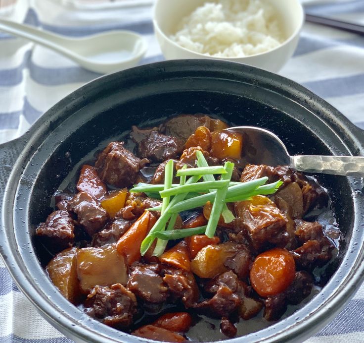 a bowl filled with meat and vegetables on top of a blue table cloth next to a spoon