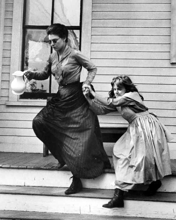 an old black and white photo of two women on the steps with one woman holding something in her hand