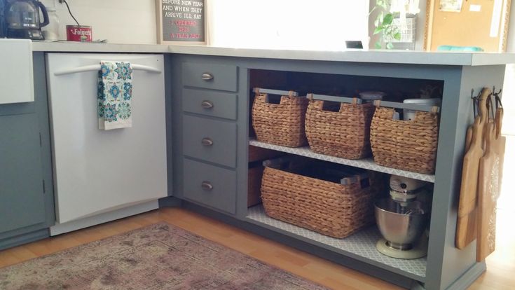 a kitchen with gray cabinets and baskets on the shelves