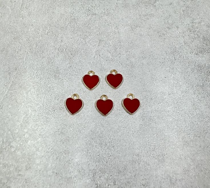 four red heart shaped charms sitting on top of a white surface