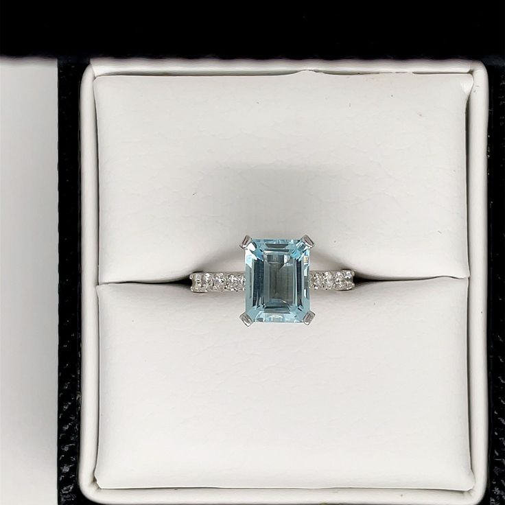 an aquamarinee and diamond ring sits in a white box on top of a black surface