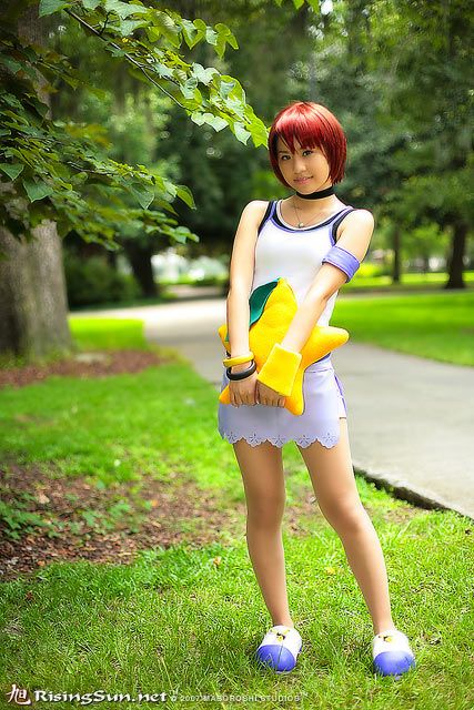 a woman with red hair is standing in the grass holding a yellow glove and wearing blue shoes