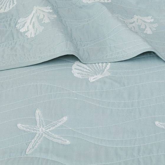 the bed is made with blue linens and white embroidered designs on it's coverlet