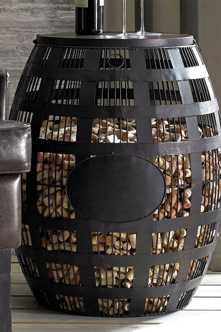 a wine bottle sitting on top of a barrel shaped firewood log holder next to a leather chair