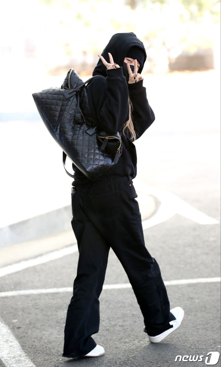 a woman walking across a parking lot with a handbag on her shoulder and peace sign in front of her face