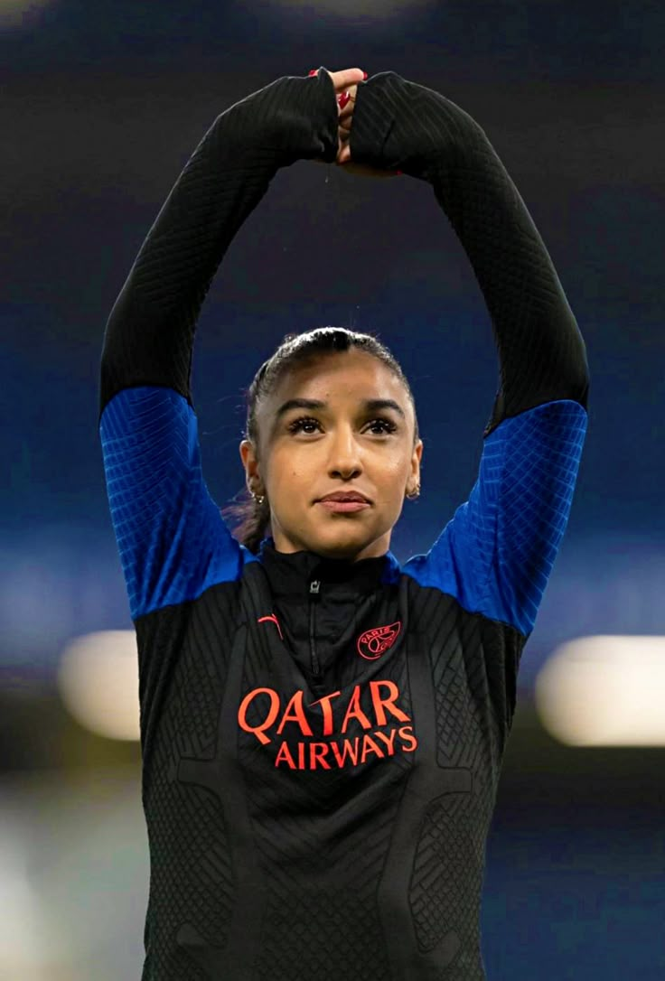 a woman holding her hands up in the air while wearing a black and blue shirt