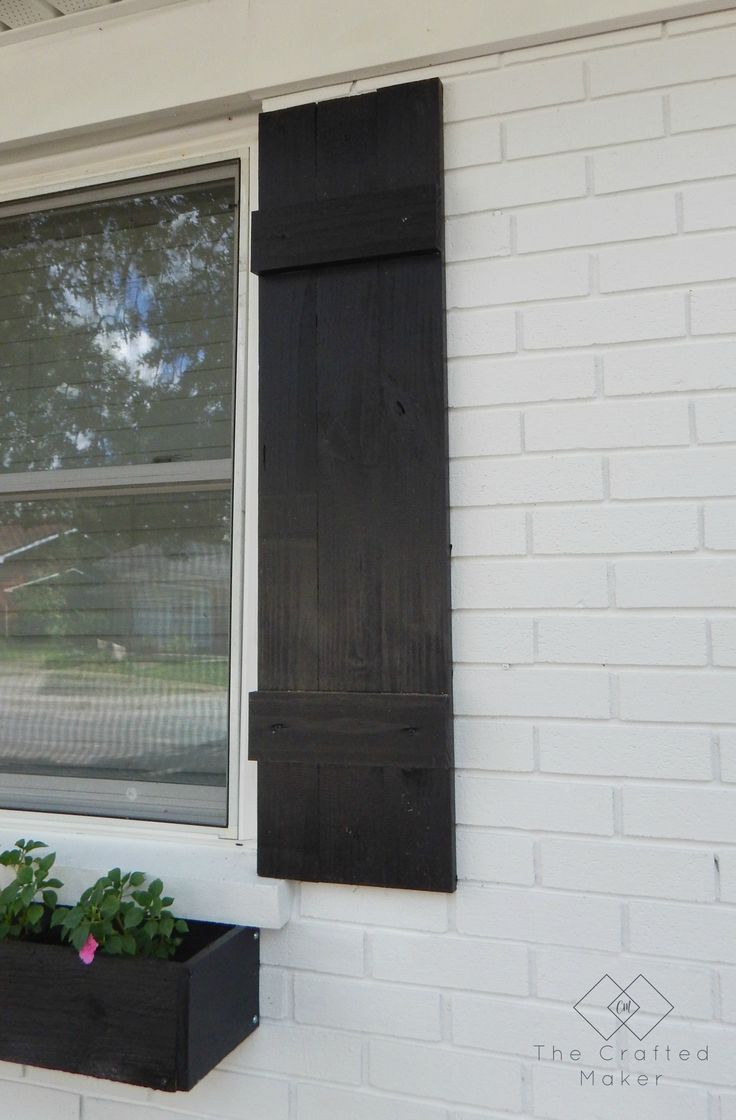 an open window on the side of a white brick building with black shutters and flower boxes