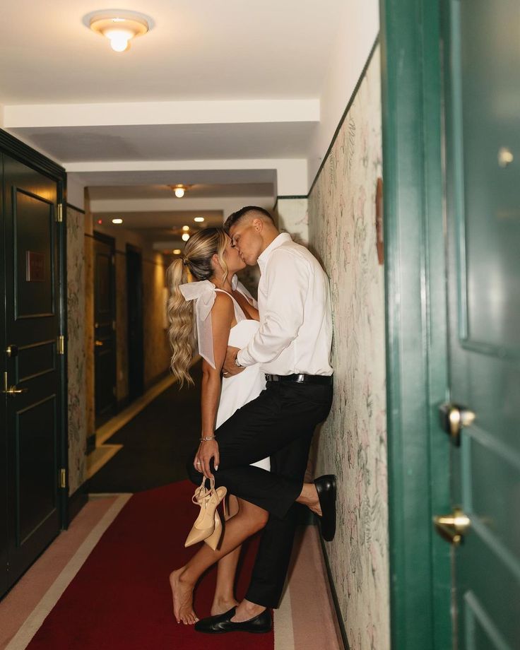 a man and woman kissing while standing next to each other on a red carpeted hallway