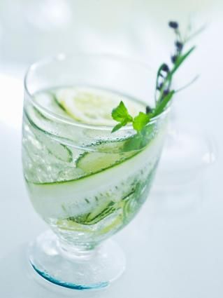 a glass filled with cucumber and water on top of a white tablecloth