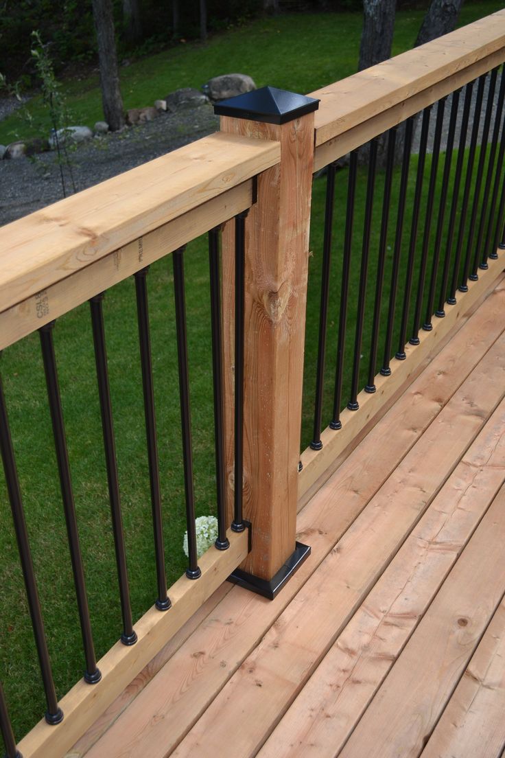 a wooden deck with black iron railings and green grass in the backgroud