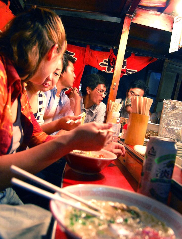 a group of people sitting at a table with food in bowls and chopsticks