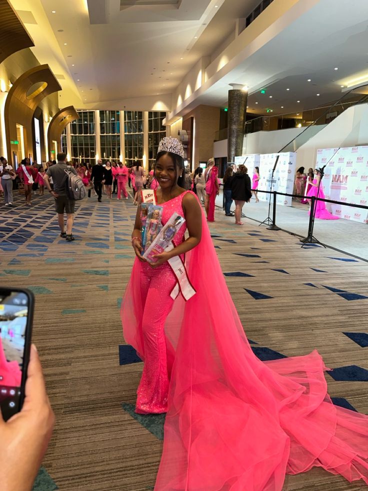 a woman in a pink dress taking a photo with her cell phone at the airport